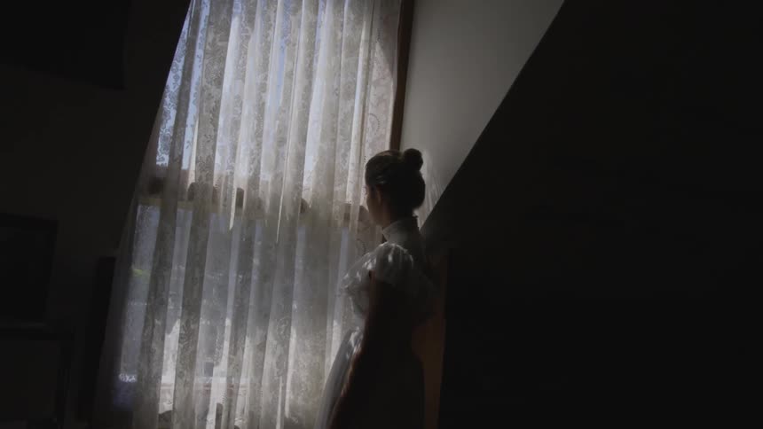 Young woman in victorian dress looks out window