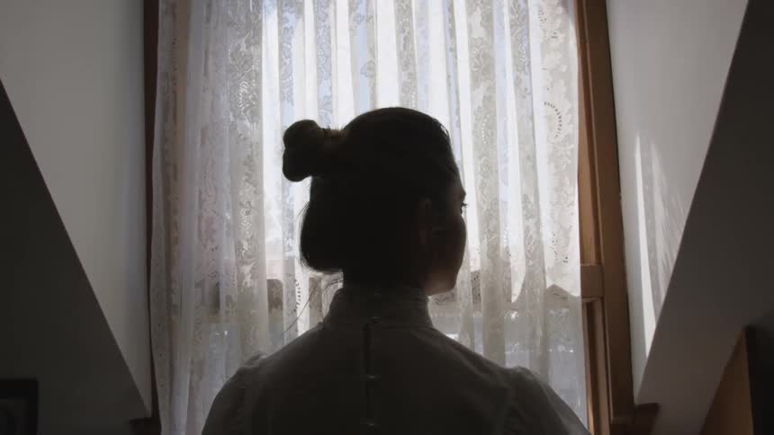 A woman stands in a narrow hallway and glances to her right
