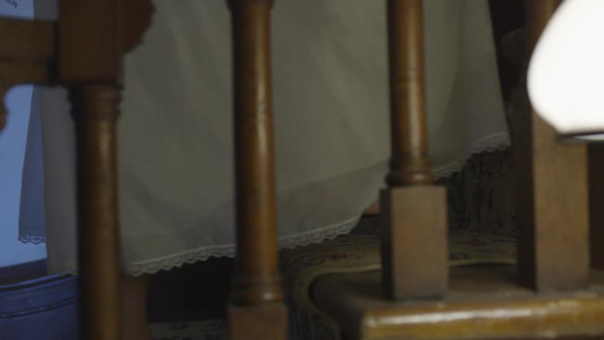 A woman in a white dress climbs the stairs inside a house