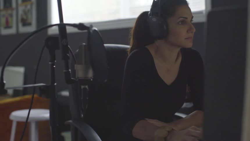 A woman wears headphones and works next to a microphone