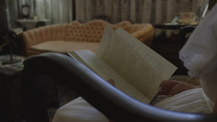 A woman in a white dress sits in a chair reading a book
