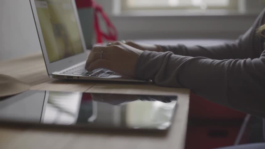 A woman types on her laptop while seated at a table
