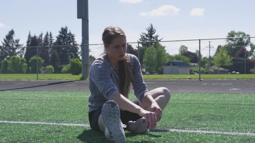 Teenage girl does stretches on athletic field