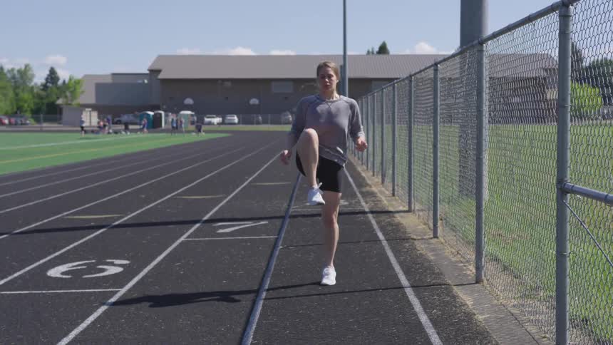 A woman does knee lifts on a track