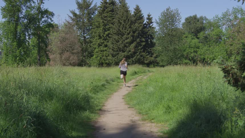 Woman running on a dirt road going to the woods