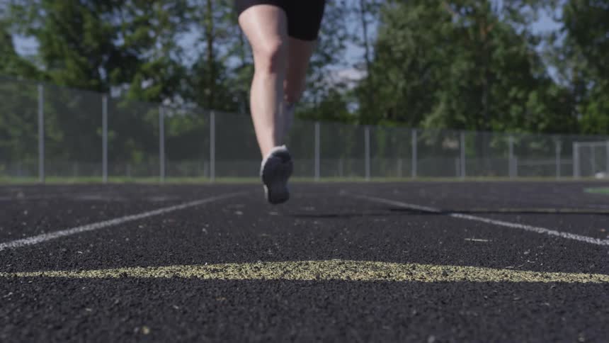 A woman running on a fenced in track in a lane crosses the yellow line