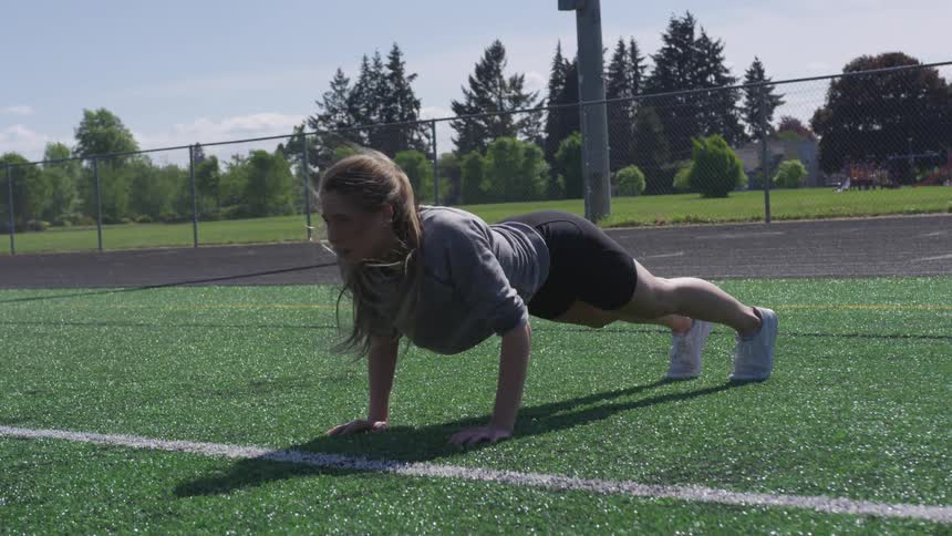 Young woman doing push ups in a football field
