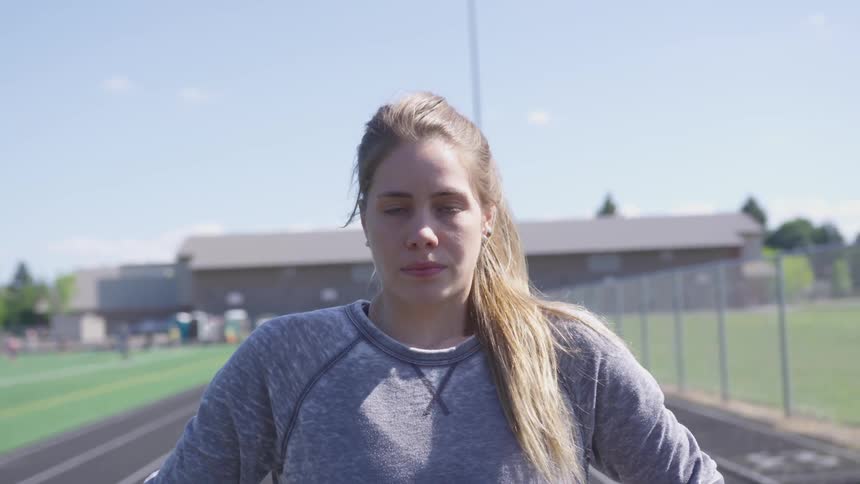 A white female on a running track taking a deep breath