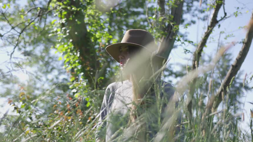 White woman wearing a hat standing in the middle of a vegetation and staring at the horizon