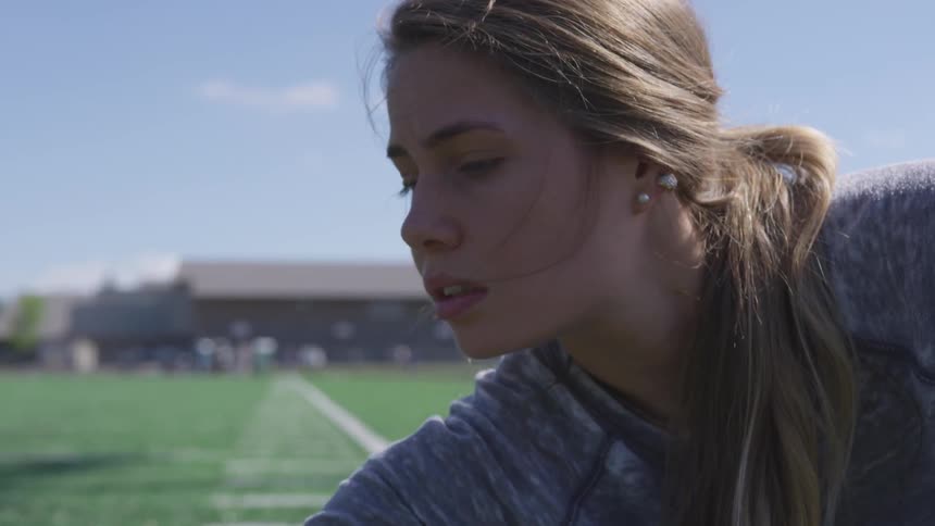 Blonde girl wearing earrings warms up in the green field on a sunny day
