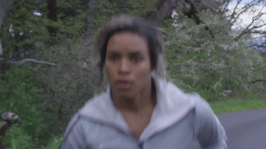 Woman wearing hoodie runs along track by woods