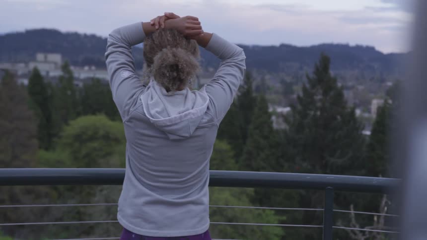 Blonde curly hair woman stretches in front of railing against the town at dusk