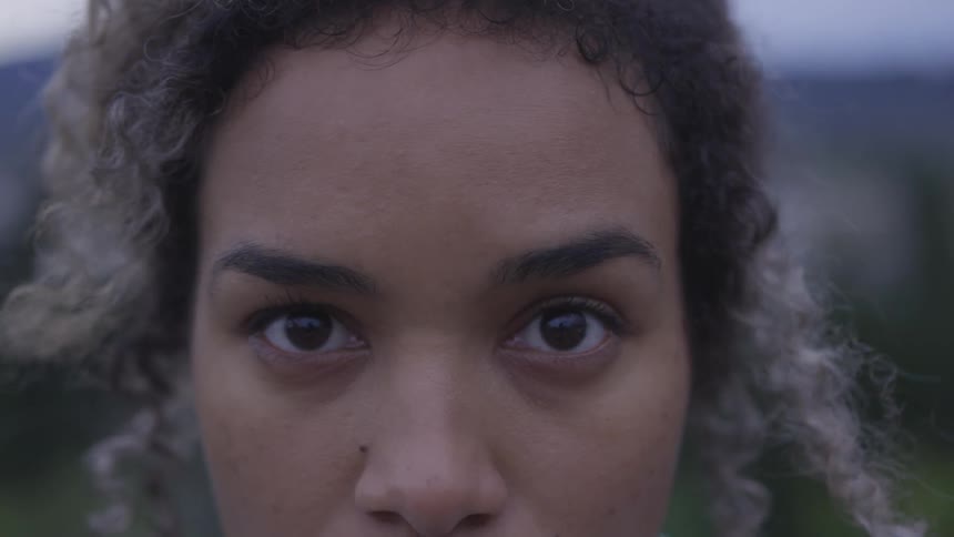 A black woman standing outdoors raising her head to look at the camera