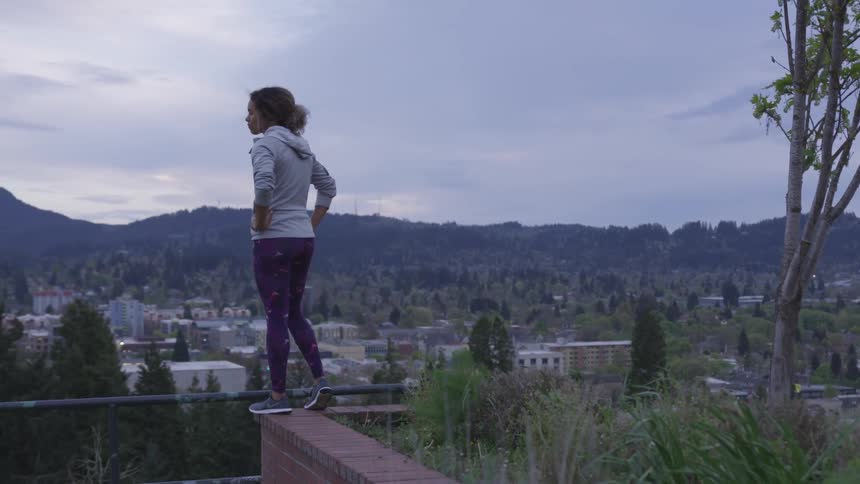 Woman standing on the edge of a planter box and looking over at city below