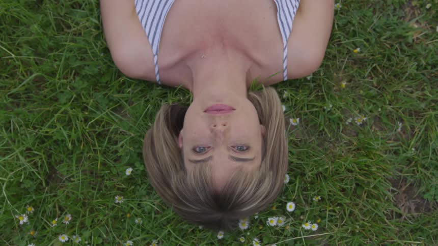 A woman lays on her back on grass and looks straight up