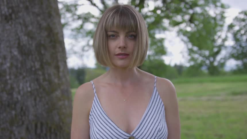 A woman looks up and poses next to a tree