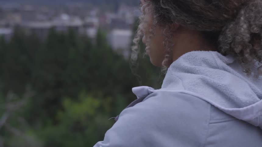 Woman stands stretching and breathing hard looking down on valley