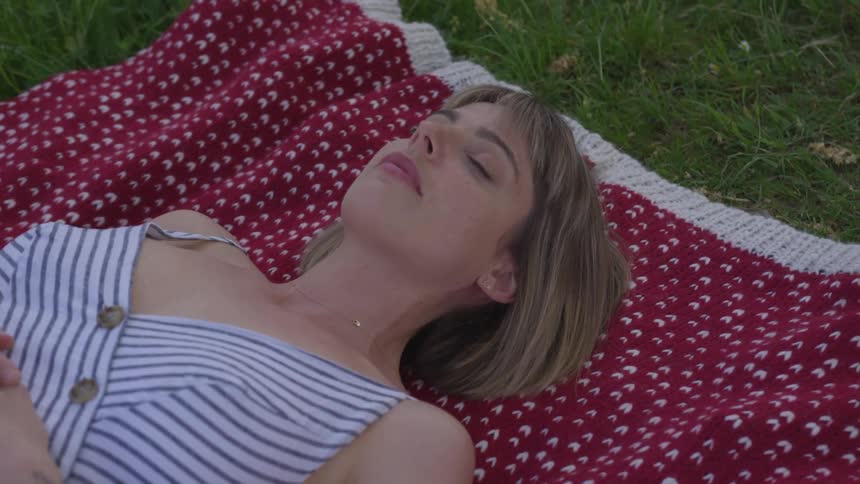 Blonde woman lies down on carpet on the grass and closes eyes in the daytime