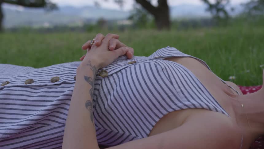Woman lies in the field of grass and clasps her hands on her chest