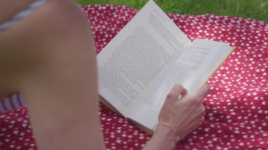 Woman reading a book while lying on top of a towel on the grass