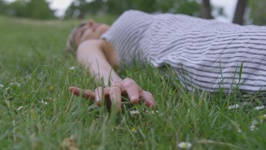 A woman laying on a field while caressing the grass with her fingers