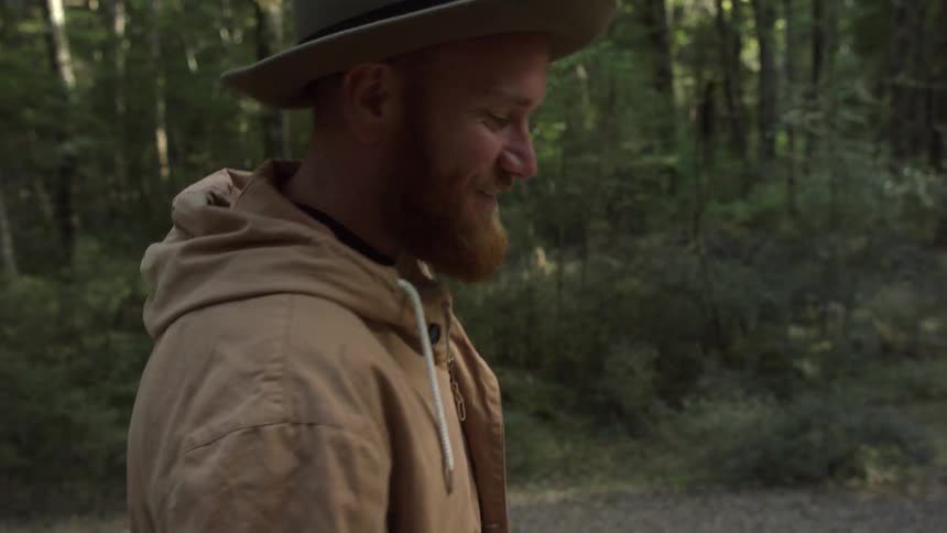 A bearded man walks through a forest trail smiling