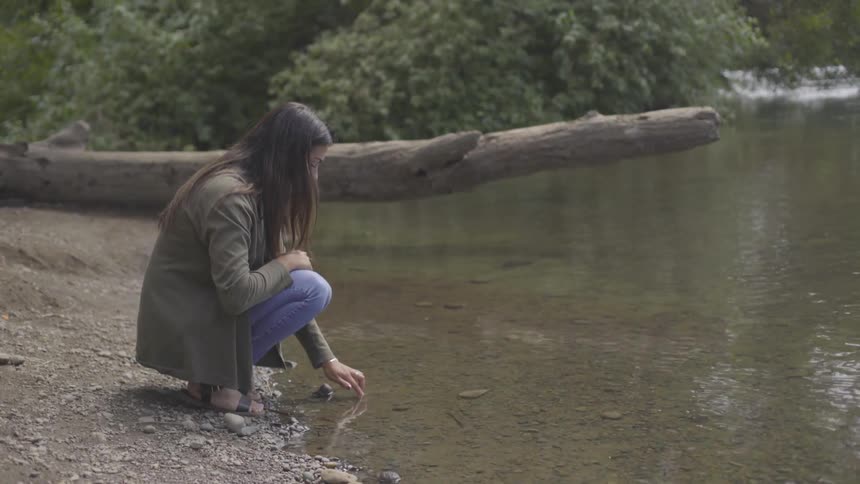 Crouching woman playing with the water next to a lake