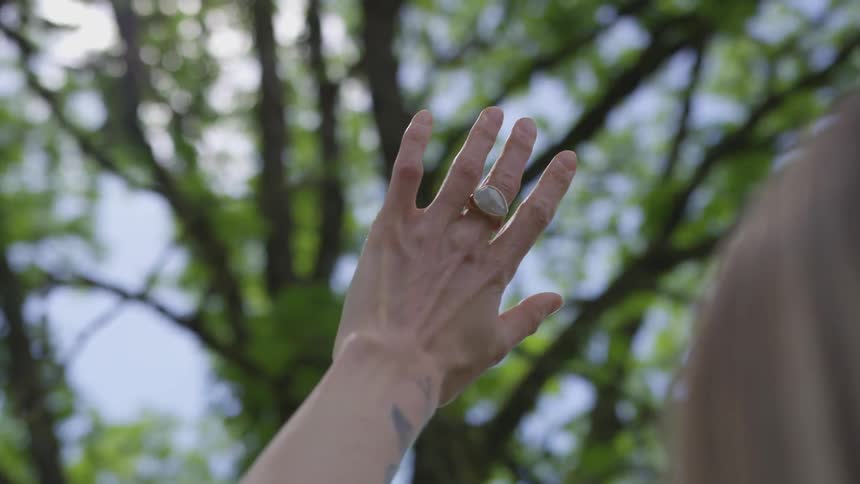 A woman placing her hand up to the sky with trees in the background