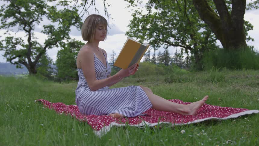 A young woman sits on a blanket and reads