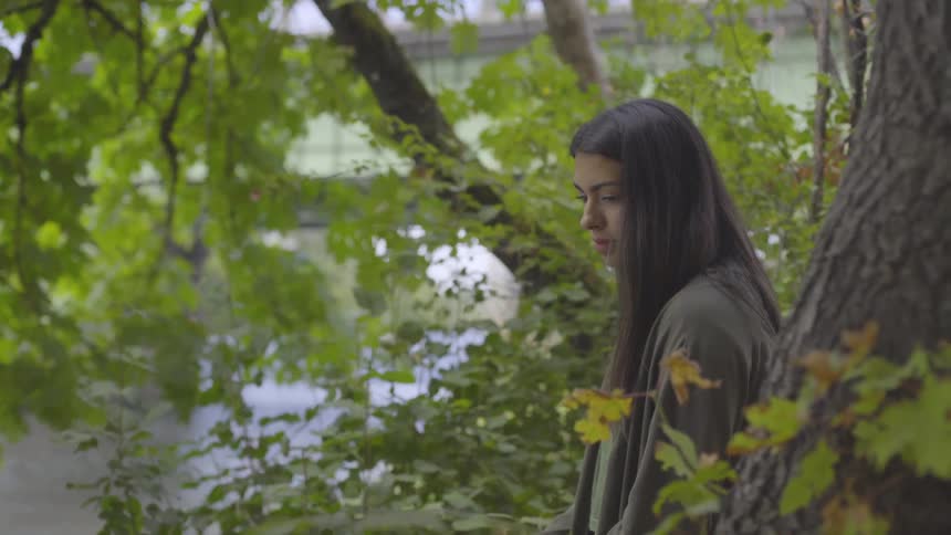 Female standing near the trees on the side of a riverbank as they ponder what to do next
