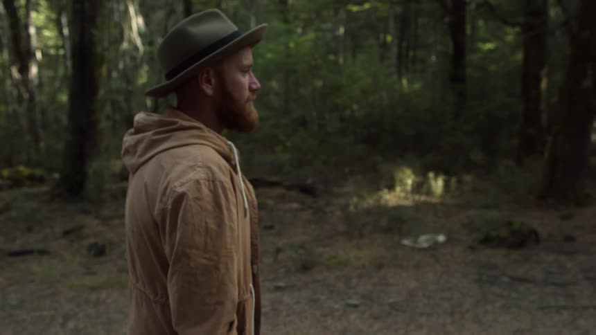 A bearded man walks down a trail in the forest