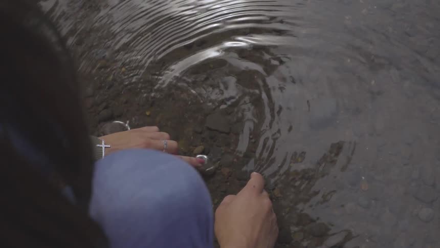 A woman swirls her finger through shallow lake water