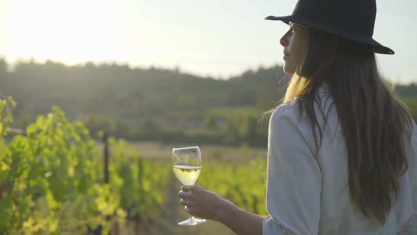 Woman holding a glass of wine walking through a vineyard