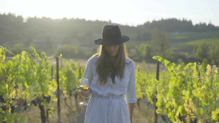 A white woman drinking wine in a vineyard