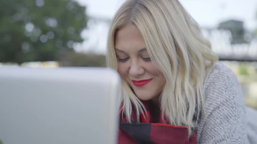 A woman outside typing on a laptop with a bridge in the background