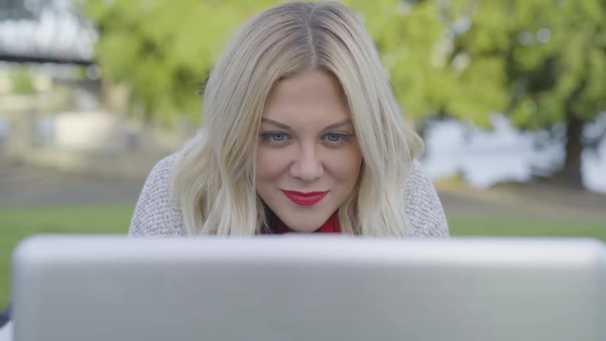 A white woman stares into a computer monitor and smiles