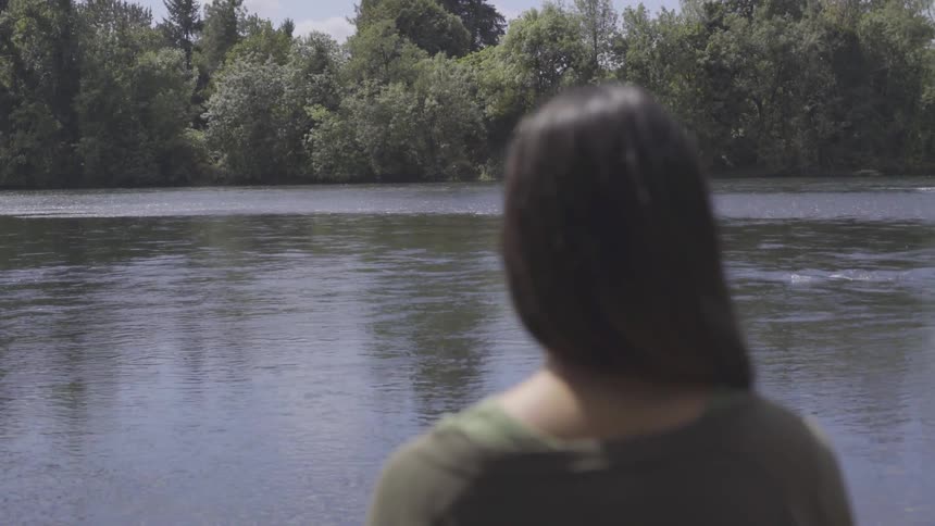 White woman looking at a river in front of her while standing next to it
