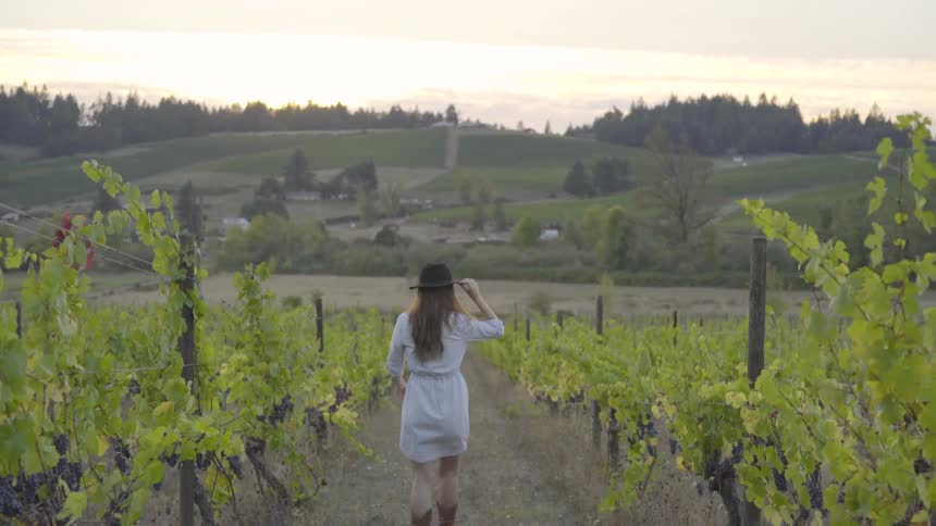 Woman walks on path near plants and puts on hat