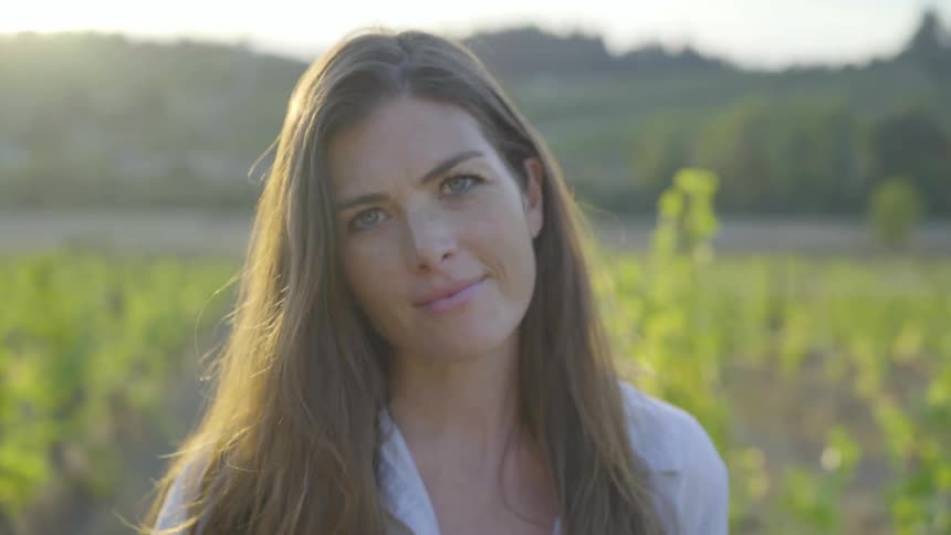 A woman in a vineyard stares into the camera lens