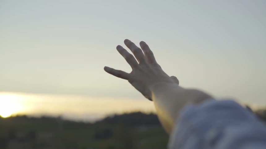 A woman is reaching their hand outdoors