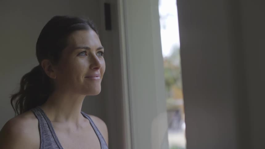 A brunette white woman looks out the window while smiling