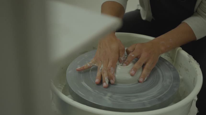 Person holds clay on pottery wheel