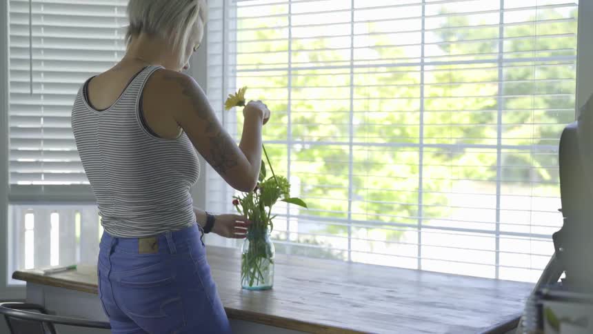 A woman indoor putting flowers in a vase