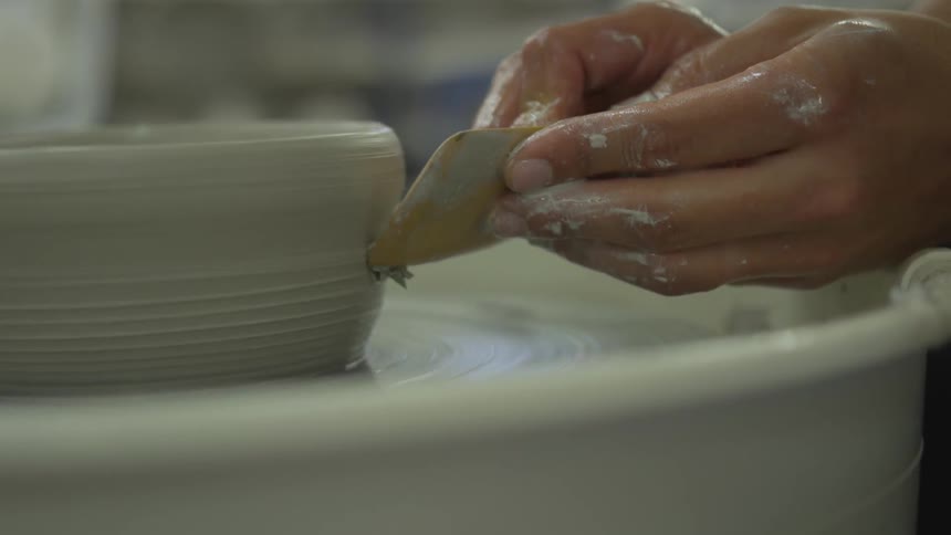 A person is shaping a clay pot with a pottery wheel and wooden tool