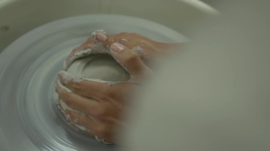 Persons hands using pottery wheel to shape clay