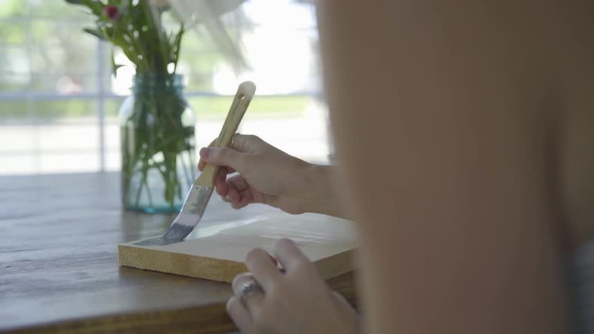 A woman paints onto a piece of wood