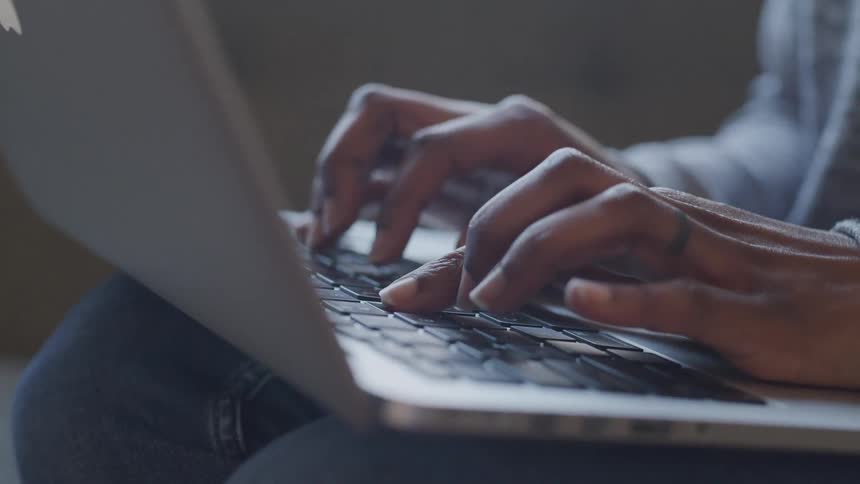 A black woman types on a computer laptop keyboard