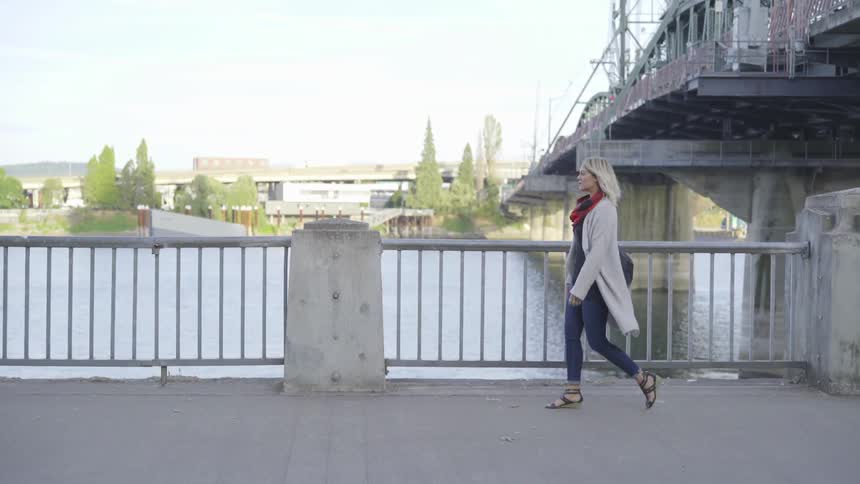 Woman and man pass along walkway near river and bridge