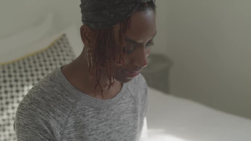 A black woman in a bedroom looks down