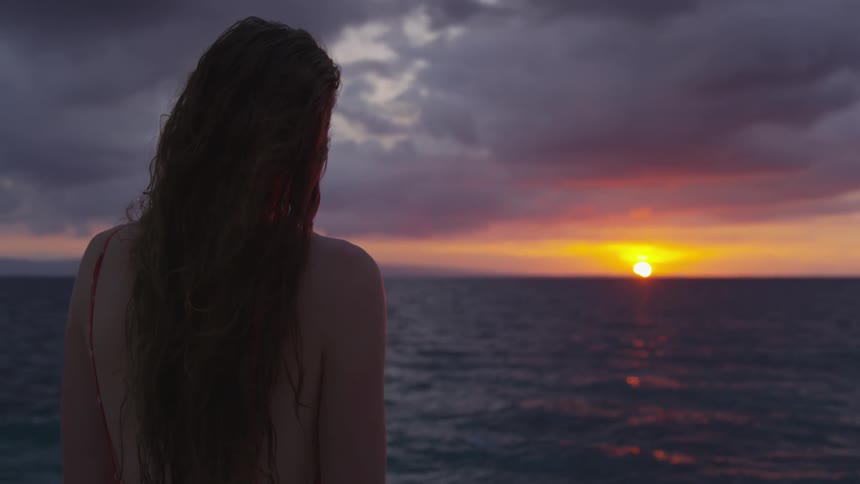 A woman standing by the ocean during sunset